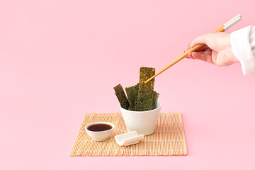 Woman eating tasty seaweed sheets on pink background © Pixel-Shot