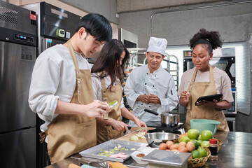 Hobby cuisine course, senior male chef in cook uniform teaches young cooking class students to peel and chop apples, ingredients for pastry foods, fruit pies in restaurant stainless steel kitchen.
