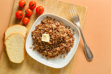 Plate of tasty buckwheat porridge, bread and tomatoes on color background