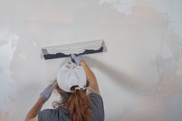 Caucasian female worker putty with a spatula with putty concrete walls in the house