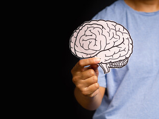 Close-up of hand holding a brain shape made from paper standing on a black background