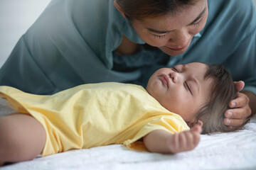 Portrait of Asian mother kissing her baby daughter sleeping on a bed, Mother's day concept