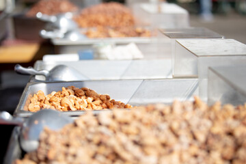 A view of several trays of roasted assorted nuts, on display at a food vendor.