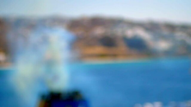 focus breath of a boat where we see the detail of a cruise ship emitting smoke and in the background the city of Mykonos with its roads and its beautiful white facades during a sunny blue summer day