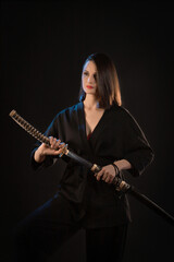 Fototapeta na wymiar A young beautiful woman in a black kimono draws a Japanese saber from its scabbard
