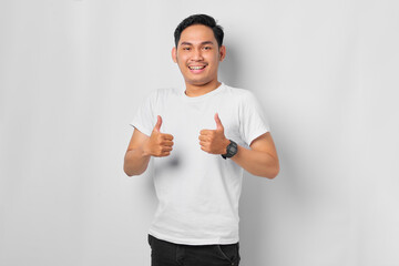 Smiling young Asian man showing thumbs up gesture, Approving expression looking at the camera isolated on white background