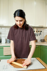 Young brunette woman knead the dough for shortcrust pastry on a baking mat, vertical