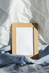 Fototapeta premium A wooden frame illuminated by the daytime sun stands on a shelf covered with linen textiles.
