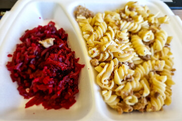 Food in disposable lunch box. Pasta with meat and salad.