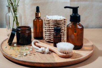 Cosmetic bottles, face brush and ear sticks on wooden tray. Spa and wellness, zero waste concept