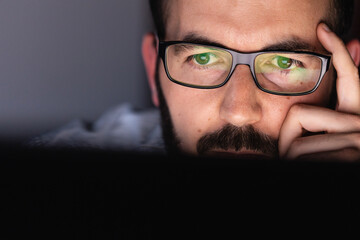 Close up of young adult programmer man face in glasses working on laptop computer at night in office - Business and freelance people concept