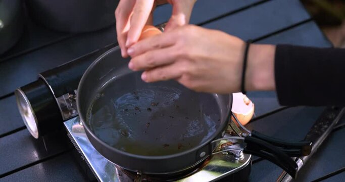 Close up shot, Selective focus, Female hands put an egg into hot oil in pan, cooking easy meal in nature park