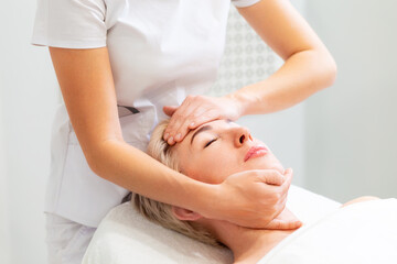 A cosmetologist massages the face of a beautiful adult woman. Rejuvenation and professional...