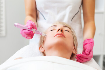 Obraz na płótnie Canvas Professional beautician in medical pink gloves does mesotherapy on the cheek of a beautiful caucasian woman. The concept of aesthetic medicine and hardware cosmetology