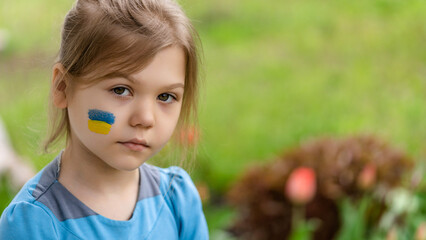 Portrait of a sad girl 8 years old with a Ukrainian flag on her face