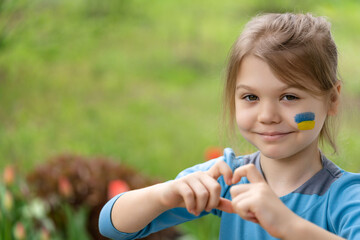 Portrait of a cheerful girl 8 years old with the Ukrainian flag on her face