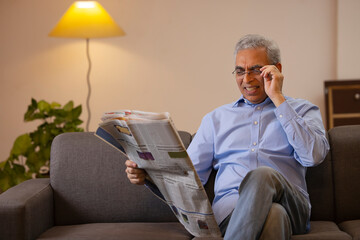 Senior man reading newspaper while sitting on sofa at home