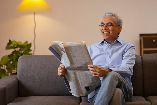 Senior man reading newspaper while sitting on sofa at home