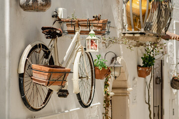 Old bicycle hanging on a white stone wall and used to hang vases and lantern in the alleys or narrow street of Mottola, Taranto, Puglia, Italy