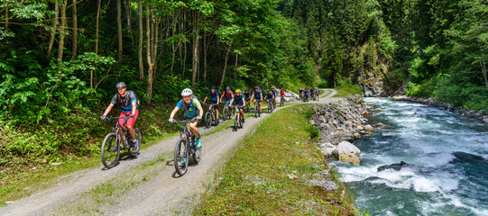 Viele Mountainbiker radeln an einem Wildbach in den Alpen entlang aufwärts
