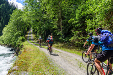 Mehrere Mountainbiker fahren an einem Wildbach in den Alpen entlang 
