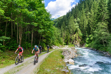 eine Gruppe Mountainbiker fährt an einem Wildbach in den Alpen entlang aufwärts
