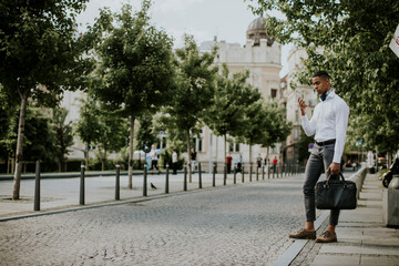 Young African American businessman using a mobile phone while waitng for a taxi on a street