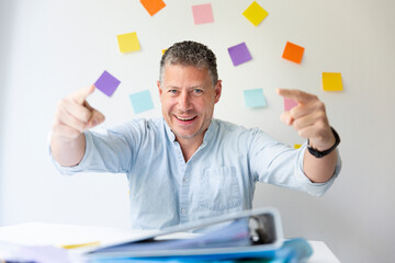 Portrait of man with blue shirt sitting at white desk full of office stuff and in the background on...