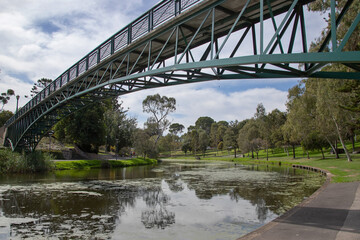 Fototapeta na wymiar Bridge over the river in the city park surrounded by green trees, cityscape