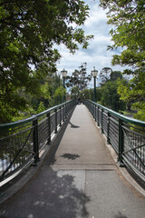 Bridge with lanterns in a city park surrounded by green trees, cityscape
