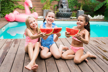 Children girls having fun and eating watermelon on poolside. Healthy food. Friendship and childhood. Outdoor leisure activity with kids by swimming pool. Summertime concept