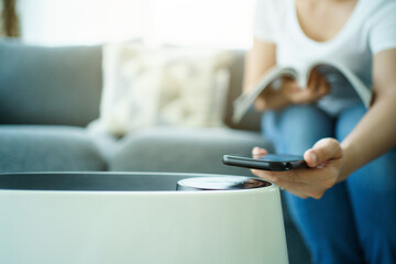 Woman control a modern air purifier through the application on a smartphone.