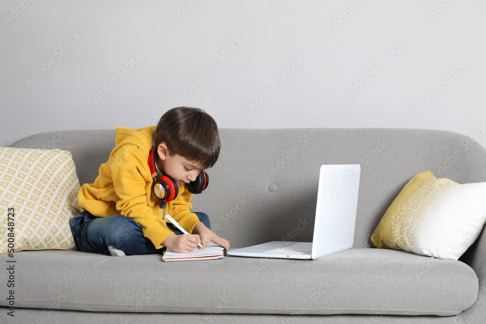 Wall mural Cute little boy with modern laptop studying online at home. E-learning