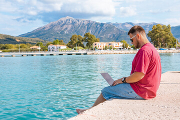 man freelancer working on laptop at city harbor bench
