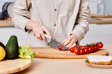 Close-up of young woman cutting cherry tomatoes with knife on cutting board at kitchen table