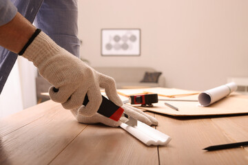 Man cutting foam crown molding with utility knife at wooden table indoors, closeup - obrazy, fototapety, plakaty
