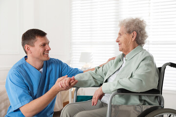 Caregiver assisting senior woman in wheelchair indoors. Home health care service - Powered by Adobe