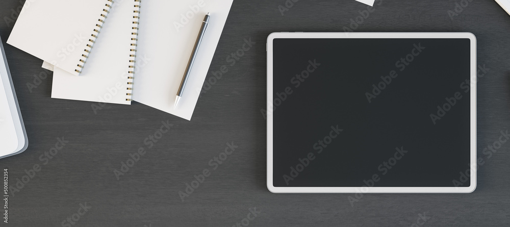 Poster tablet with blank screen is on top of dark wooden office desk table with supplies, above view. mock 