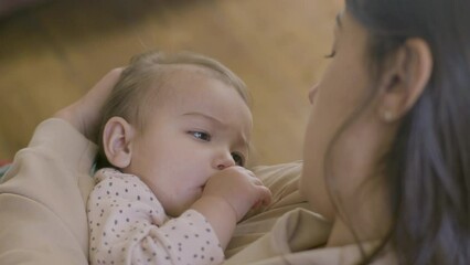 Closeup shot of young mother putting her baby daughter to sleep by singing lullaby and stroking her hair gently. Long-haired beautiful woman watching her baby girl falling asleep. Motherhood concept