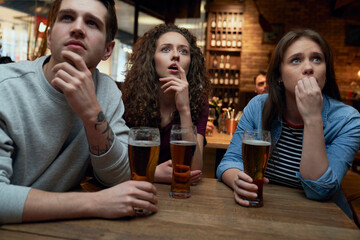 Nervous soccer fans having beer and watching a match together in a pub