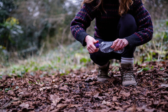 Young woman picking up plastic bottle in forest