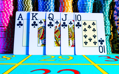 Royal flush, straight flush from ten to ace on the background of game chips for playing poker. Casino gambling concept. Poker set on a blue gaming table close up. Entertainment in an elite poker club.
