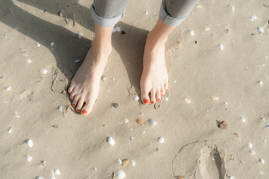 Woman standing barefeet on sand with seashells at beach