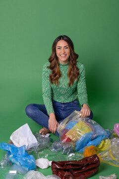 Happy young woman sitting with plastic waste against green background