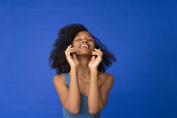 Young woman with eyes closed laughing against blue background