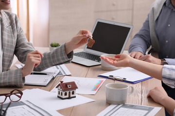 Real estate agent giving house key to young couple in office, closeup. Mortgage concept