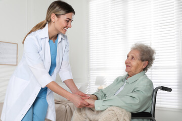 Young caregiver assisting senior woman in wheelchair indoors. Home health care service - Powered by Adobe