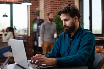 Entrepreneur man sitting at desk in startup office brainstorming ideas while working at marketing project analyzing company turnover on laptop. Diverse businesspeople planning business collaboration