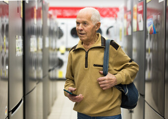 elderly grayhaired man pensioner looking refrigerator at counter in showroom of electrical appliance hypermarket department