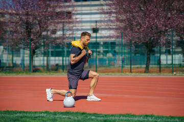 Obraz premium Muscular young man exercising with heavy weight bag in the sport stadium. Sporty man working out with heavy weight bag.